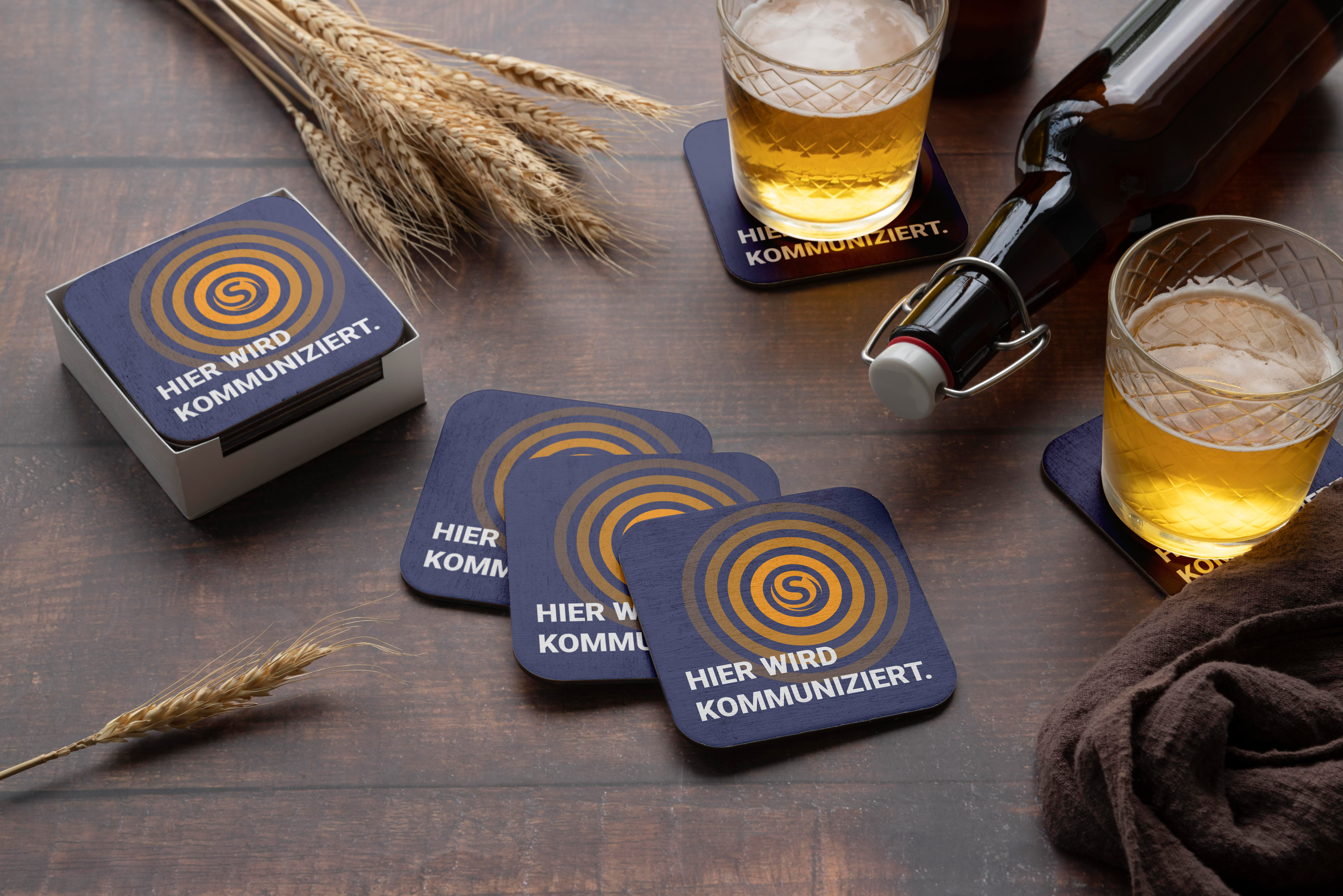 Untersetzer mit Branding auf einem Tisch neben Gläsern mit Getränken in einer Innenraumszene